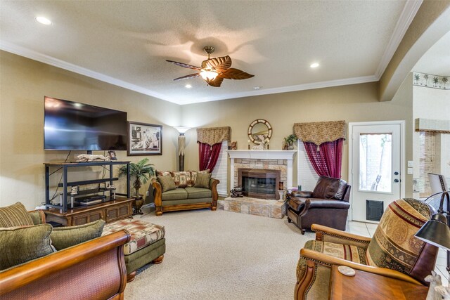 living room with carpet floors, crown molding, a textured ceiling, ceiling fan, and a stone fireplace