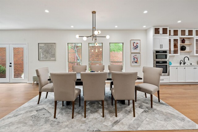 dining room featuring french doors, sink, light wood-type flooring, and an inviting chandelier