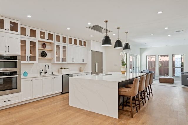 kitchen with stainless steel appliances, sink, light hardwood / wood-style floors, a kitchen island with sink, and white cabinetry