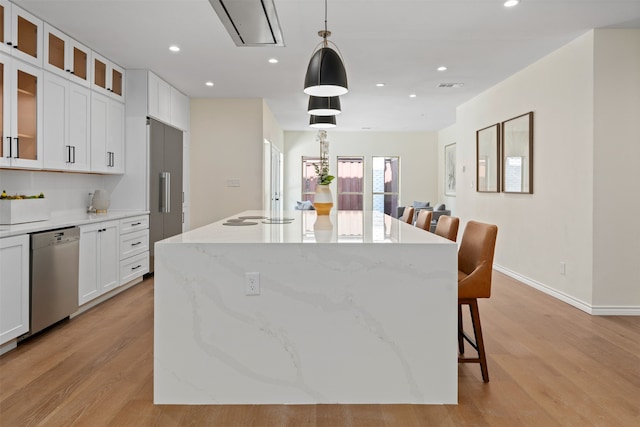 kitchen with light hardwood / wood-style flooring, white cabinets, light stone counters, an island with sink, and stainless steel dishwasher