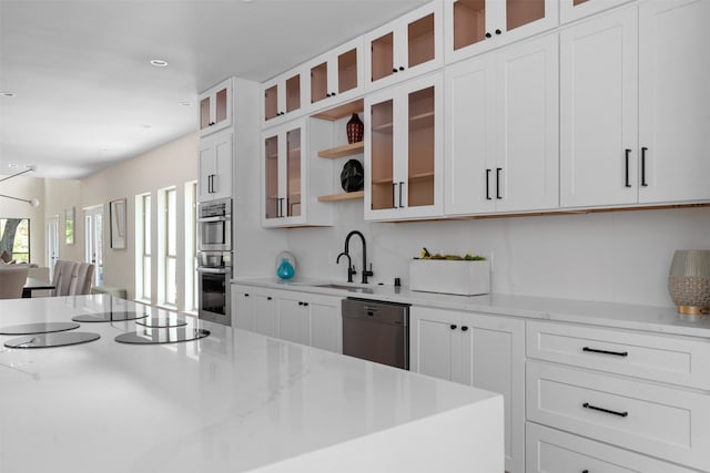 kitchen with appliances with stainless steel finishes, white cabinetry, light stone countertops, and sink