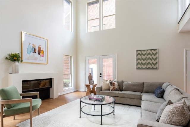 living room featuring a fireplace, french doors, light wood-type flooring, and a high ceiling