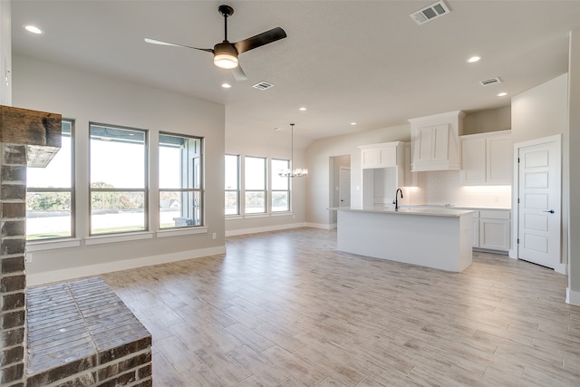 kitchen with white cabinets, ceiling fan with notable chandelier, light hardwood / wood-style flooring, and a kitchen island with sink