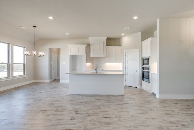 kitchen featuring appliances with stainless steel finishes, pendant lighting, a center island with sink, a notable chandelier, and white cabinetry