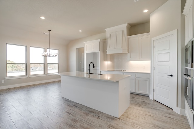 kitchen with sink, white cabinets, an island with sink, and decorative light fixtures