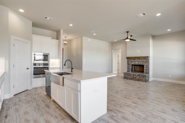 kitchen featuring white cabinetry, a kitchen island with sink, a fireplace, and stainless steel appliances