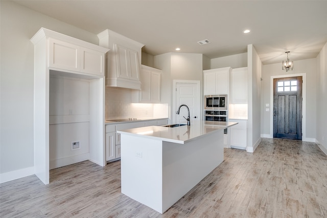 kitchen featuring stainless steel appliances, white cabinetry, a kitchen island with sink, and sink