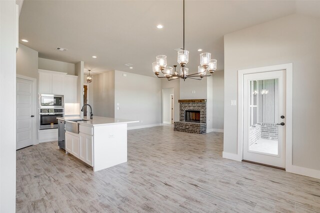 kitchen featuring sink, stainless steel appliances, a fireplace, white cabinets, and a center island with sink