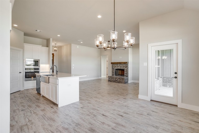 kitchen with built in microwave, sink, decorative light fixtures, a center island with sink, and oven