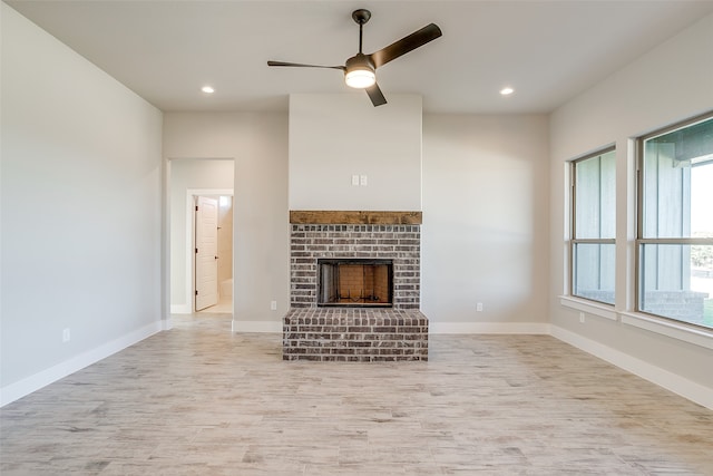 unfurnished living room featuring a brick fireplace, ceiling fan, plenty of natural light, and light wood-type flooring