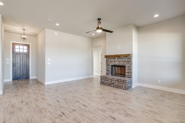 unfurnished living room with ceiling fan with notable chandelier, light hardwood / wood-style floors, and a brick fireplace