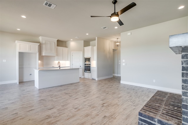 kitchen featuring appliances with stainless steel finishes, ceiling fan with notable chandelier, light hardwood / wood-style flooring, white cabinetry, and an island with sink