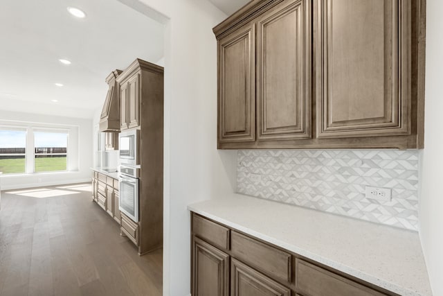 kitchen featuring tasteful backsplash, light stone countertops, oven, and light wood-type flooring