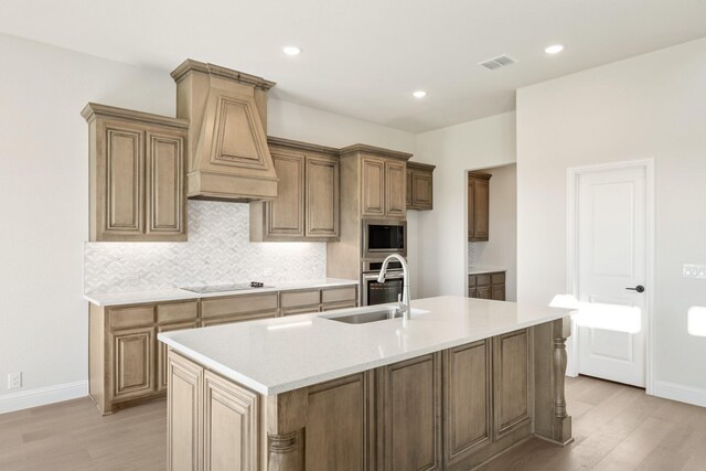 kitchen featuring appliances with stainless steel finishes, custom exhaust hood, sink, light hardwood / wood-style flooring, and an island with sink