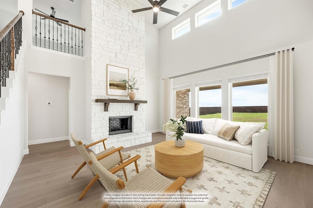 living room with a stone fireplace, ceiling fan, light hardwood / wood-style flooring, and a towering ceiling