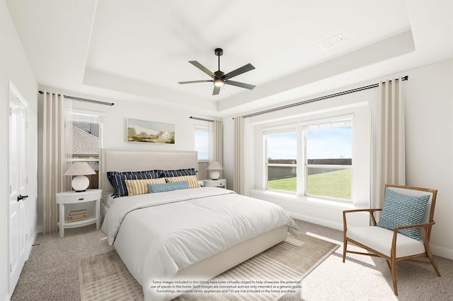 carpeted bedroom with a raised ceiling and ceiling fan