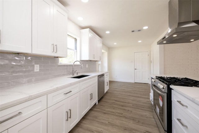 kitchen featuring sink, white cabinetry, light stone counters, ventilation hood, and appliances with stainless steel finishes