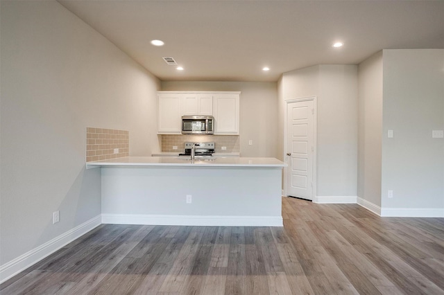 kitchen with white cabinetry, appliances with stainless steel finishes, light hardwood / wood-style flooring, and kitchen peninsula