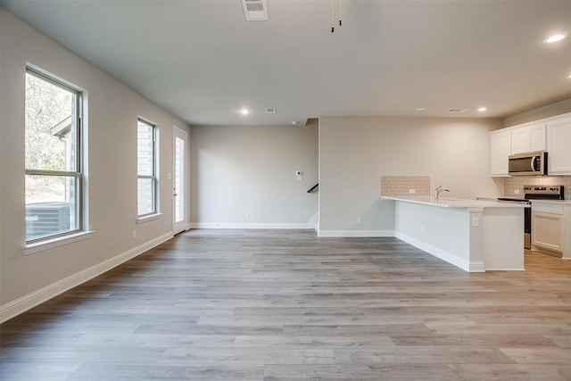 kitchen with tasteful backsplash, appliances with stainless steel finishes, light hardwood / wood-style floors, and white cabinets