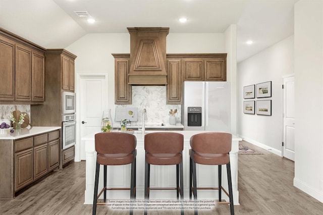 kitchen featuring tasteful backsplash, a center island with sink, light hardwood / wood-style floors, and appliances with stainless steel finishes