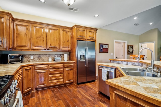 kitchen featuring stainless steel appliances, sink, vaulted ceiling, backsplash, and dark wood-type flooring