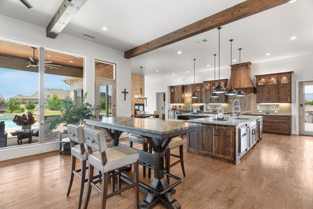 kitchen with beamed ceiling, a center island with sink, backsplash, hardwood / wood-style flooring, and ceiling fan