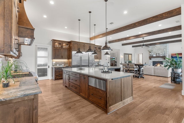 kitchen with a large island with sink, light hardwood / wood-style flooring, a stone fireplace, and beam ceiling