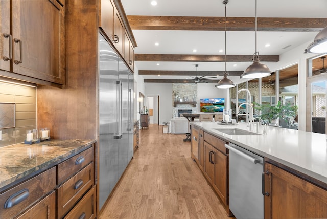 kitchen featuring a fireplace, light hardwood / wood-style flooring, appliances with stainless steel finishes, beamed ceiling, and ceiling fan