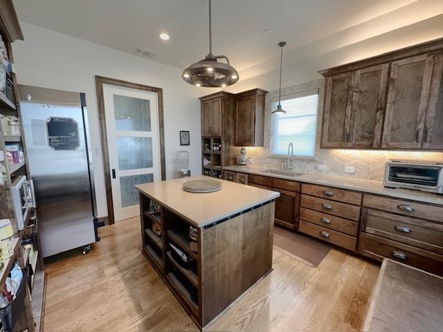 kitchen featuring pendant lighting, backsplash, a center island, sink, and light hardwood / wood-style floors