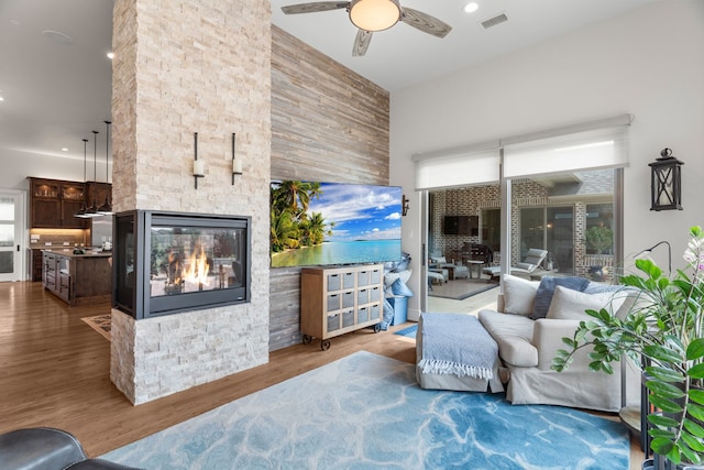 living room with hardwood / wood-style floors, ceiling fan, and a stone fireplace