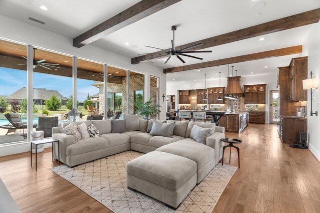 living room with a healthy amount of sunlight, ceiling fan, beam ceiling, and light hardwood / wood-style floors