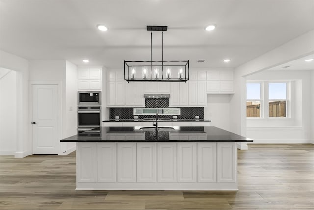 kitchen featuring built in microwave, white cabinetry, pendant lighting, oven, and a kitchen island with sink