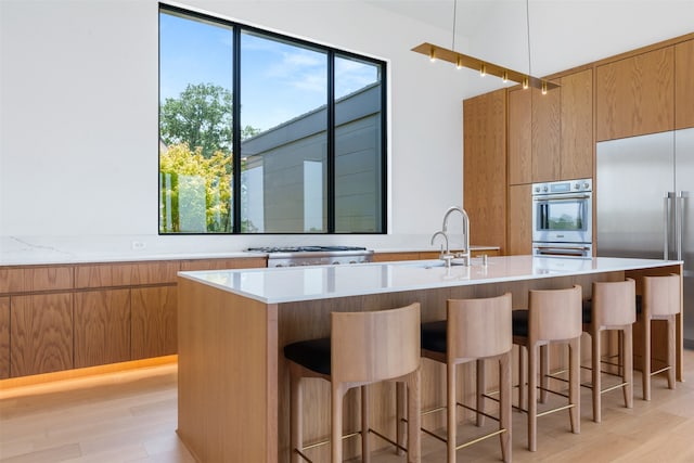 kitchen with a kitchen island with sink, sink, light wood-type flooring, and stainless steel built in refrigerator