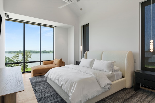 bedroom featuring light hardwood / wood-style flooring, a wall of windows, ceiling fan, and a water view