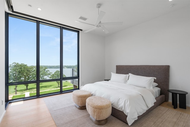 bedroom with ceiling fan, a water view, a wall of windows, and light hardwood / wood-style floors