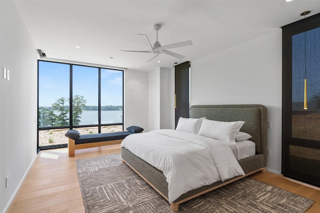 bedroom featuring wood-type flooring, expansive windows, ceiling fan, and a water view