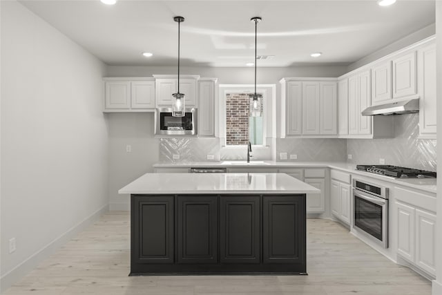 kitchen with stainless steel appliances, a center island, light hardwood / wood-style flooring, decorative light fixtures, and sink