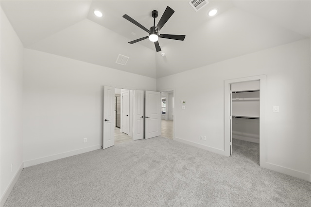 unfurnished bedroom featuring a closet, lofted ceiling, ceiling fan, a walk in closet, and light carpet