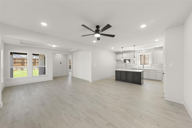 unfurnished living room featuring light wood-type flooring, sink, and ceiling fan