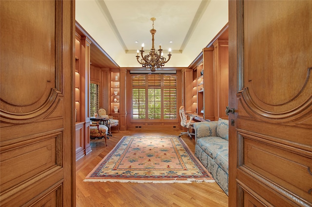 sitting room featuring light hardwood / wood-style floors, a tray ceiling, wooden walls, and an inviting chandelier