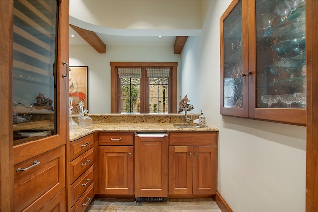 kitchen featuring beam ceiling, kitchen peninsula, sink, and light stone counters