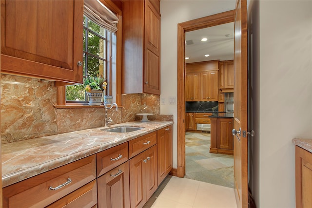 kitchen featuring light stone countertops, light tile patterned floors, tasteful backsplash, and sink