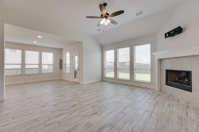 unfurnished living room with lofted ceiling, a healthy amount of sunlight, a tiled fireplace, and light hardwood / wood-style floors