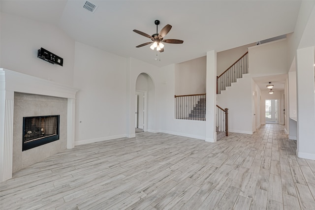 unfurnished living room featuring ceiling fan, lofted ceiling, a tile fireplace, and light wood-type flooring