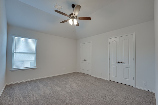 unfurnished bedroom featuring two closets, ceiling fan, light carpet, and vaulted ceiling