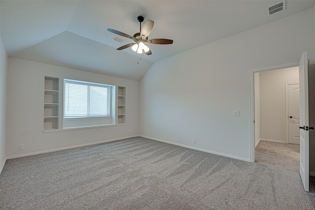 carpeted empty room with built in shelves, vaulted ceiling, and ceiling fan