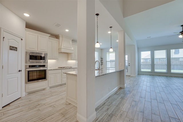 kitchen with custom exhaust hood, stainless steel appliances, ceiling fan, light hardwood / wood-style floors, and white cabinetry