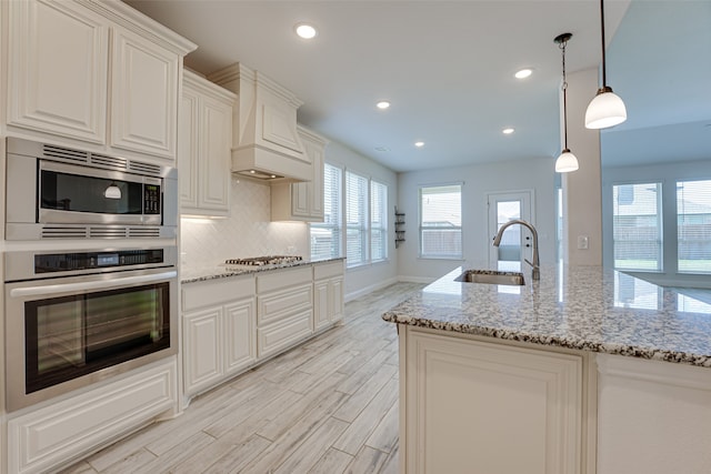 kitchen featuring light stone countertops, appliances with stainless steel finishes, sink, decorative light fixtures, and light hardwood / wood-style floors