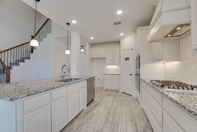 kitchen featuring white cabinets, a center island with sink, sink, appliances with stainless steel finishes, and custom range hood