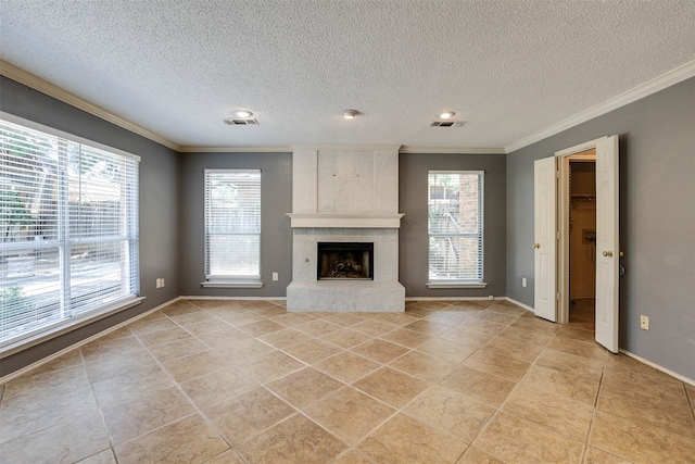 unfurnished living room with a tiled fireplace, crown molding, light tile patterned floors, and a textured ceiling